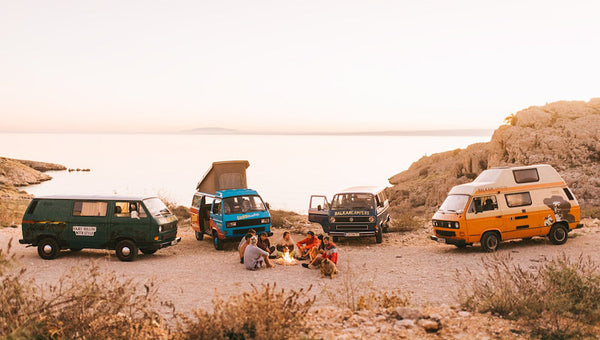 friends with campervans on road trip sit around a fire