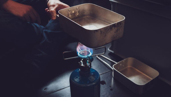 person cooks over fire with propane tank from lpg generator